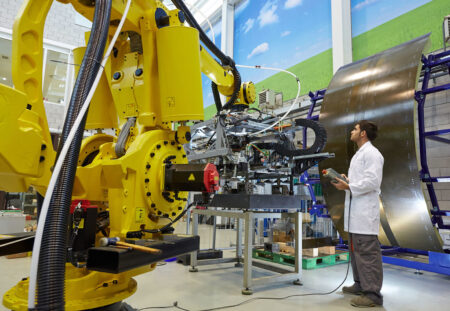 A man in a white lab coat operates a large industrial machine in a large industrial facility